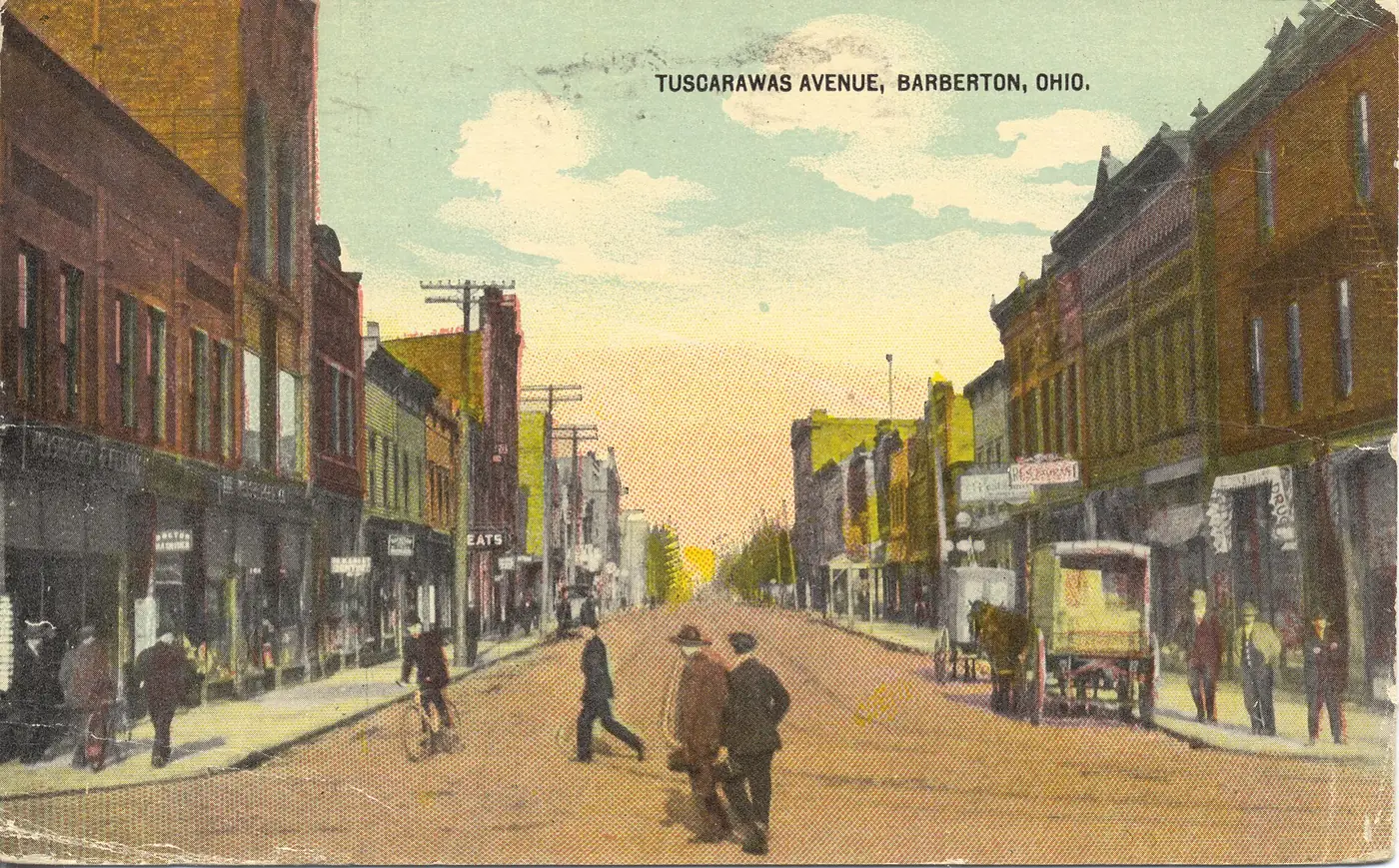 Hand-tinted postcard of Tuscarawas Avenue, Barberton, with shop fronts and people in the street, about 1910